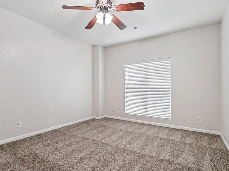 Bright, spacious bedroom with plush carpet, large window with blinds, and a modern ceiling fan. Bright, spacious bedroom with plush carpet, large window with blinds, and a modern ceiling fan.