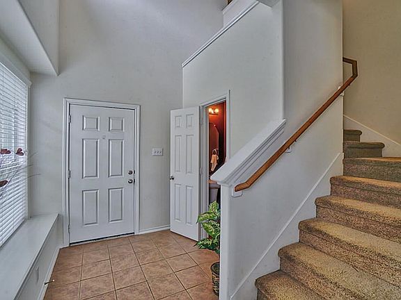 View of the front door from the living room.  Title flooring welcomes you into your home.  The half bathroom is nestled just under the stair.  Natural lighting shines bright through the window.