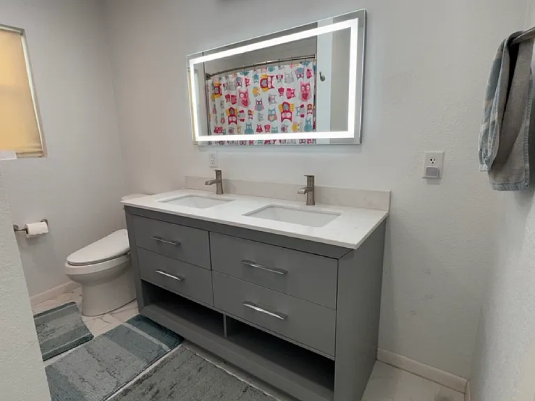 The fully renovated second bathroom features a spacious double-sink vanity, an integrated LED-backlit mirror, beautiful marble-look tile, and a premium Kohler soaking tub with a full shower setup.