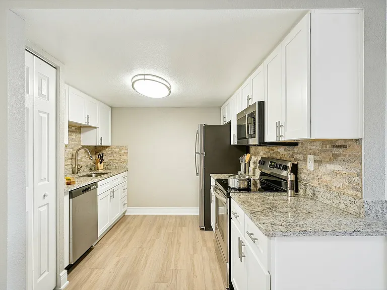 Modern kitchen with sleek white cabinets, granite countertops, and stainless steel appliances, exuding a bright and inviting ambiance.