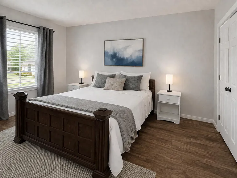 Spacious bedroom with a large window, wood-look flooring, and a bed flanked by nightstands with matching lamps.