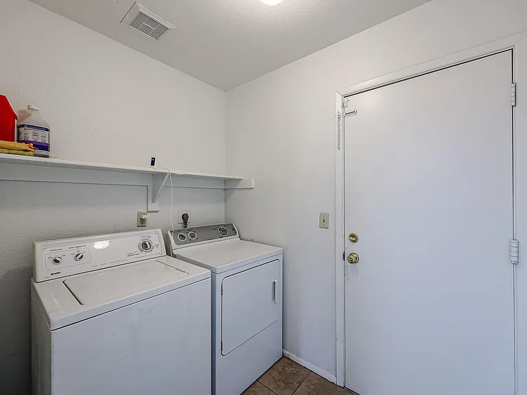 Dedicated laundry area with side-by-side washer and dryer, plus a wall shelf for detergent and supplies.