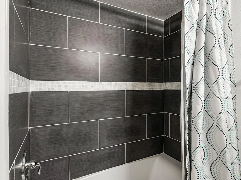 Tiled tub/shower surround with accent band and a shower curtain, offering an easy-care bathing space.