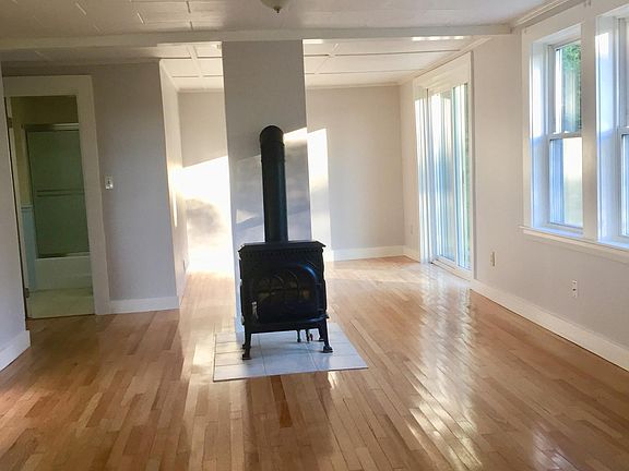 living room with Jotul propane heater. Slider door onto deck with privacy fence. Bathroom entrance through the door to the left of heater.