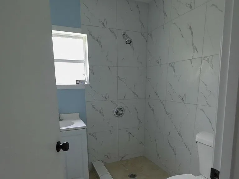 Walk-in shower with marble-look tile surround, plus a single-sink vanity and window for ventilation and natural light.