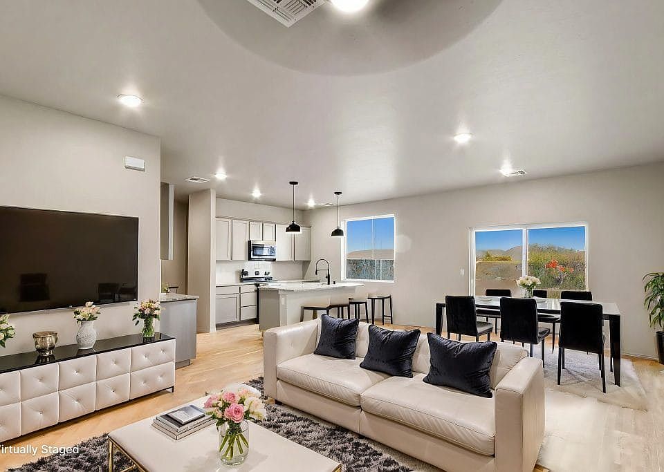 A modern, open-concept living and dining area features a white sofa with navy pillows, a large TV, a