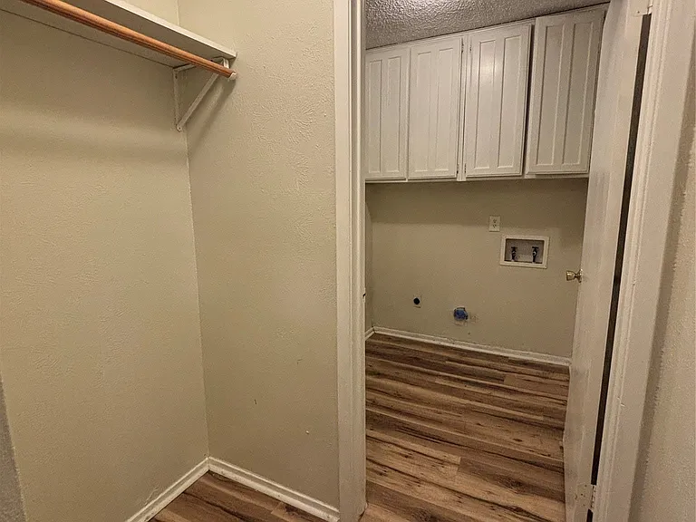 Wood-finish flooring throughout, leading to a utility space with white shaker cabinetry and a ceiling-mounted light fixture