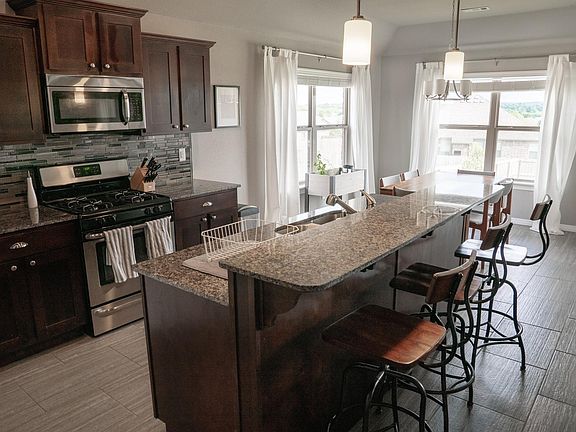 Bright Kitchen with granite countertops, stainless steel appliances (oven, stove, microwave, fridge/freezer, dishwasher), south-facing windows, and dark wood cabinets.