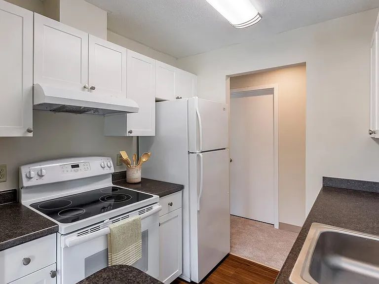 Classic Package I kitchen with white appliances, dark laminate countertops, white cabinetry, and hard surface flooring