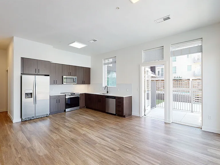 Apartment kitchen with stainless steel appliances, dining and living room with wood-style flooring and balcony or patio.