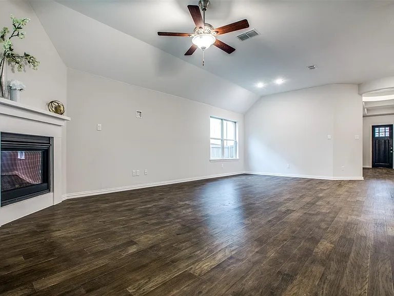 Spacious living area featuring wood-finish flooring, a white mantel fireplace, a vaulted ceiling, and recessed lighting