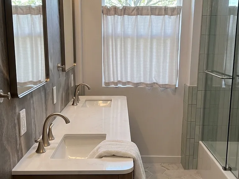 Upstairs bathroom with double vanity, custom tile statement wall and glazed window with cafe curtain for privacy.