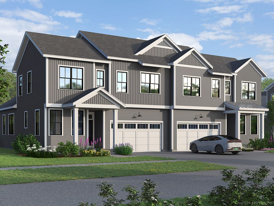 A modern two-story duplex with gray siding, two white garage doors, and a driveway featuring a parke