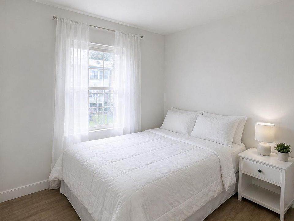 Serene bedroom with a full-size bed, nightstand lighting, and a large window with sheer curtains for natural light.