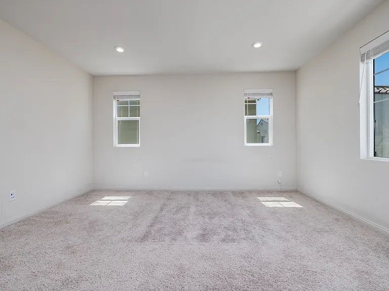 Spacious master bedroom with multiple windows providing abundant natural light. Features soft carpet flooring, recessed lighting, and a serene atmosphere_perfect for creating a relaxing private retreat.