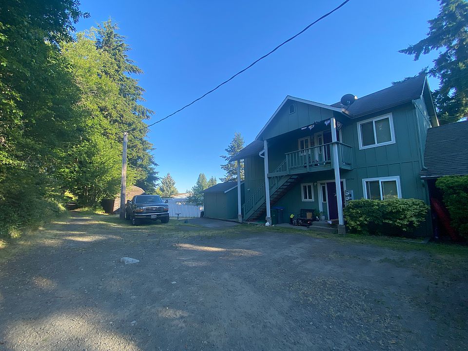 Upper and lower apartments, parking area bordered by a trail and native plants & blackberry bushes to the left.
