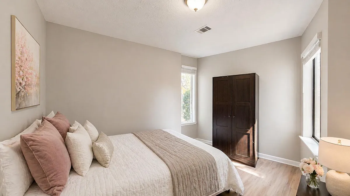 Spacious bedroom with natural light, neutral walls, and room for storage, featuring a wardrobe and bedside table. - Branch Dr