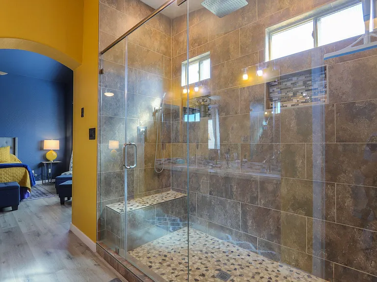 Spacious walk-in shower with glass enclosure, large-format tile, built-in bench, and high windows for natural light.