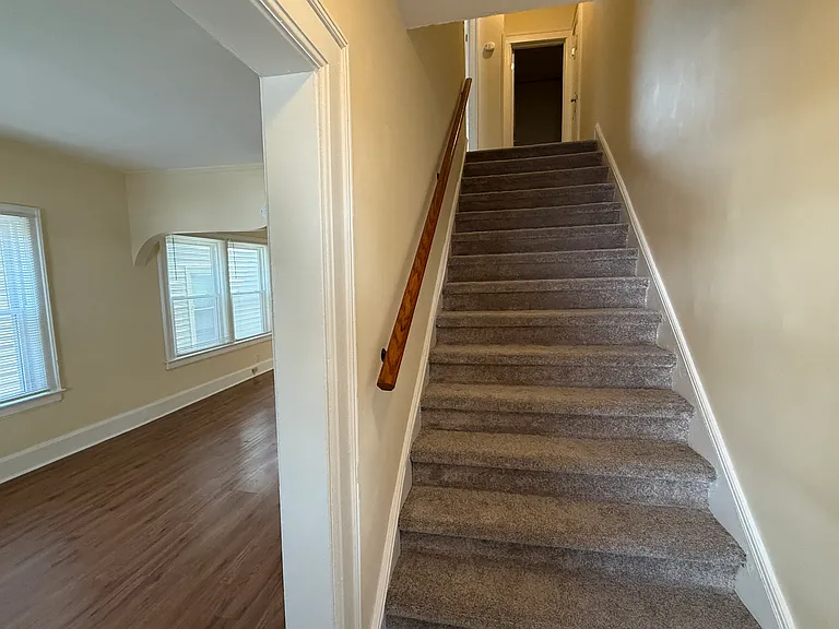 As you enter through the front door, you face the stairwell with brand new carpet (installed 2025). To the left is the living room. Bathroom shown at the top of the stairs. Stairwell is very wide compared to most multi-unit homes of this era.