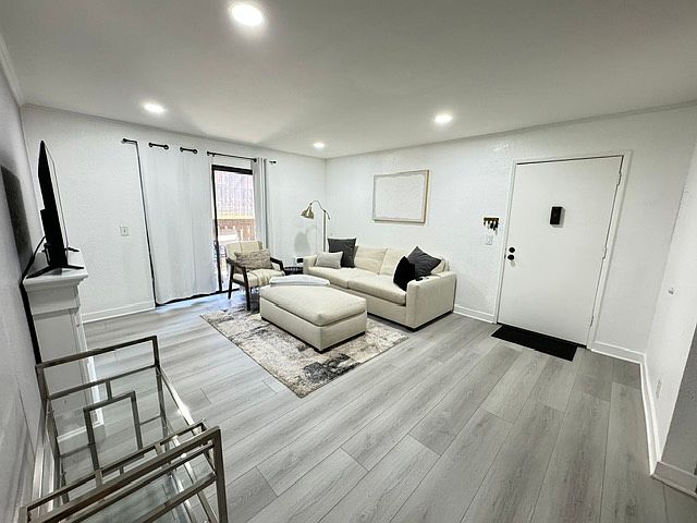Living room with newly installed hardwood floors. Natural light from glass doors, in-wall AC unit.