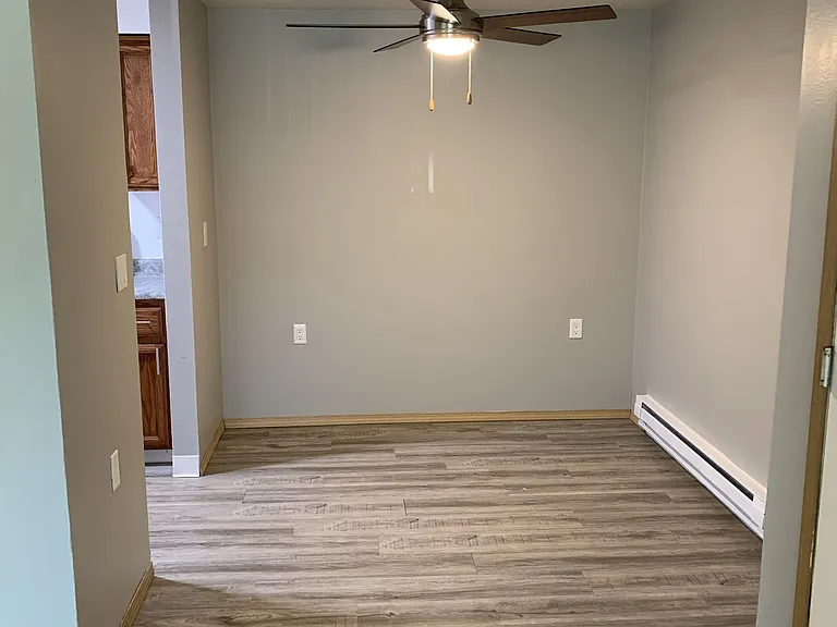 Cozy dining area featuring wood-style flooring, neutral walls, and a modern ceiling fan with lighting. Offers a defined space perfect for dining or entertaining, with an open feel connecting to the nearby kitchen.