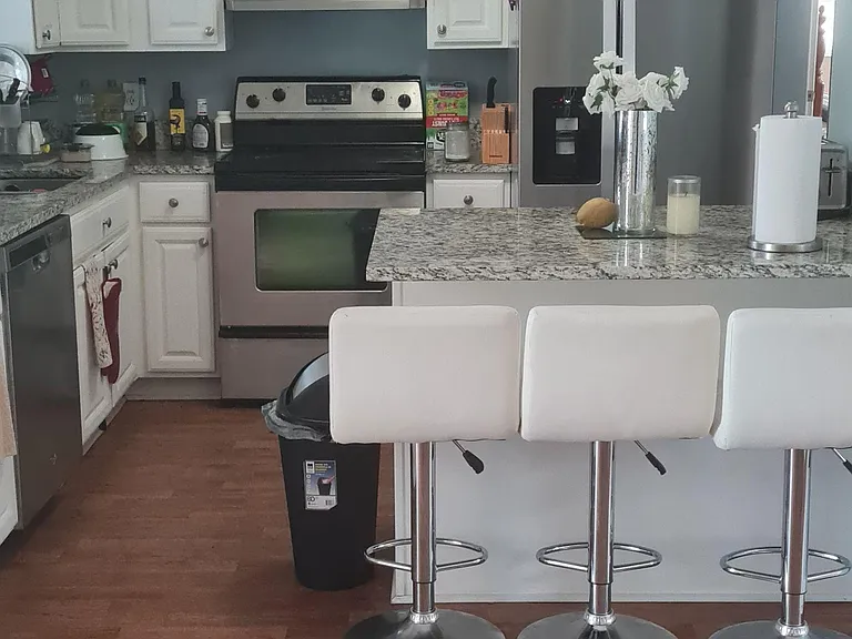 Kitchen with white cabinetry, stainless appliances, and a granite-topped breakfast bar with seating for three.