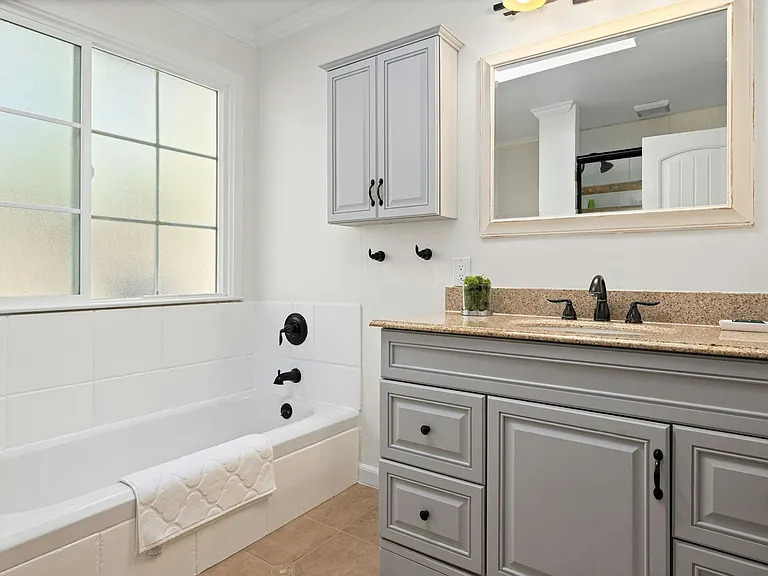 Elegant and functional featuring a soft gray vanity, soaking tub, and large window for natural light, this bathroom blends style and serenity for everyday comfort.