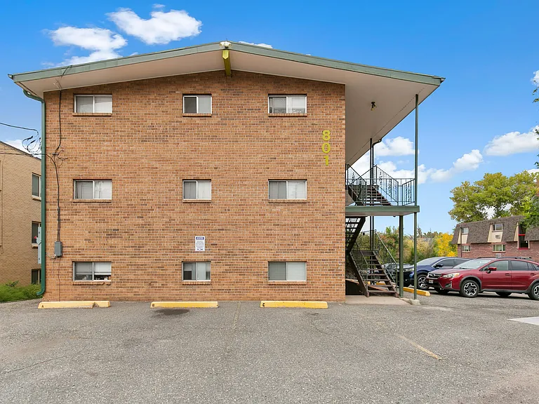 Charming brick apartment building with outdoor staircase, ample parking, and clear blue skies.