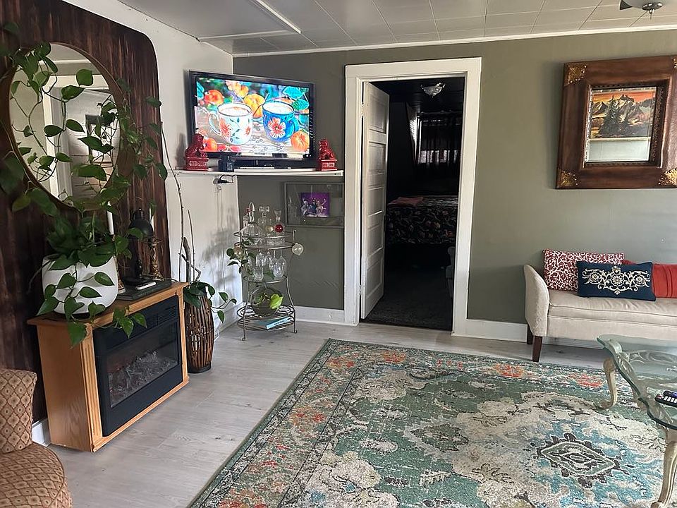 East side of living room with electric fireplace, flat screen tv, and the bedroom is thru the door that is open in this picture