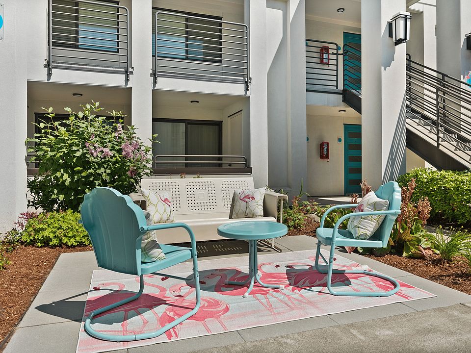 Charming outdoor seating area with turquoise chairs and a flamingo-themed rug, set against a modern apartment backdrop.