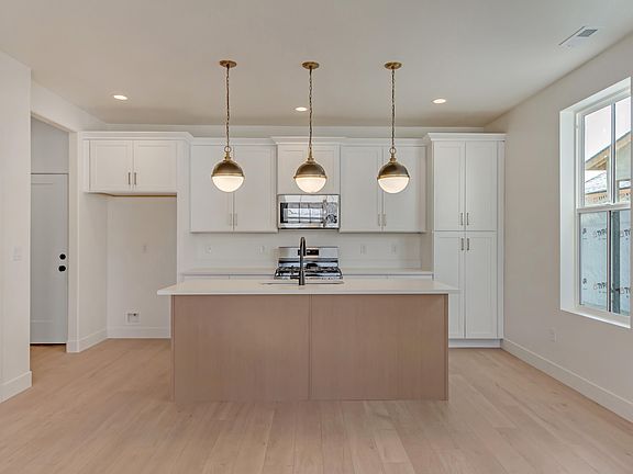 Modern kitchen with white cabinets, a central island with a sink, three pendant lights, built-in ove