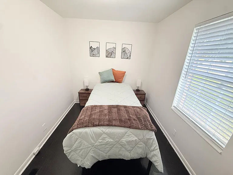 Neat single bedroom with a twin bed, matching nightstands, and a large window with blinds for natural light and privacy.