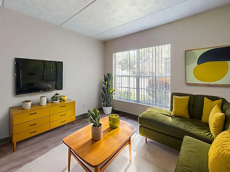 Bright and stylish living room with a green sectional sofa, vibrant yellow accents, and modern decor, bathed in natural light from a large window.