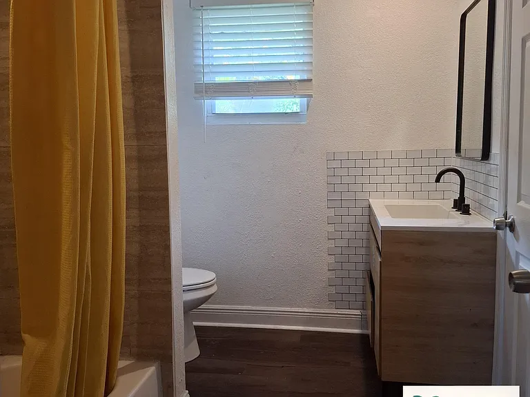Full bathroom with tub/shower combo, updated vanity, and window with blinds for natural light and ventilation.