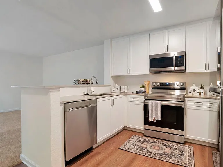 Kitchens with stainless steel appliances, beige quartz countertops, white cabinetry, and hard surface flooring