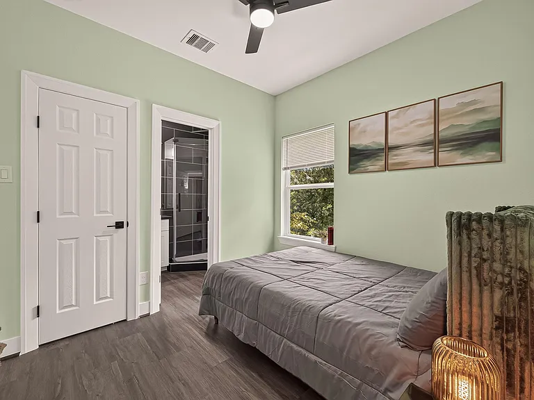 Furnished bedroom with a ceiling fan, window, and easy access to an en-suite bath with a tiled shower.