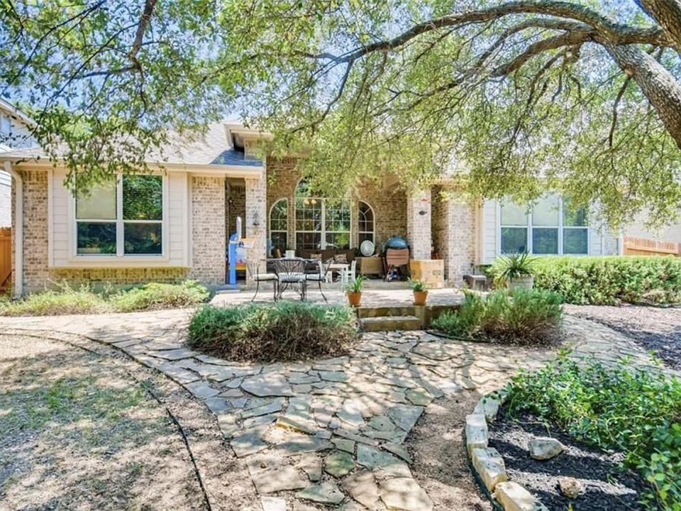 Backyard view with stone patio shaded by mature trees.