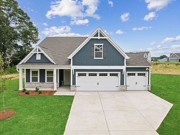 A blue house with a white garage door is sitting on top of a lush green field.