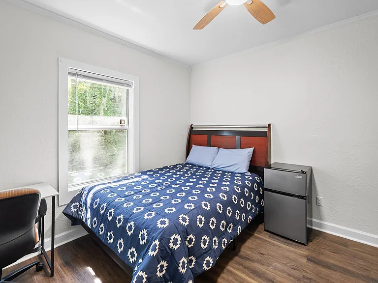 Bedroom with a double bed, ceiling fan, large window, and a mini fridge for convenient in-room storage.