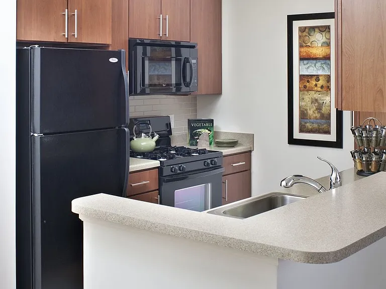 Classic Package II kitchen with dark oak cabinetry, beige laminate countertops, beige subway tile backsplash, black appliances and hard surface flooring