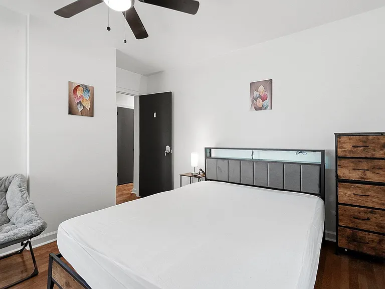 Furnished bedroom with a full bed, dresser, accent chair, ceiling fan, and easy access to the hallway.