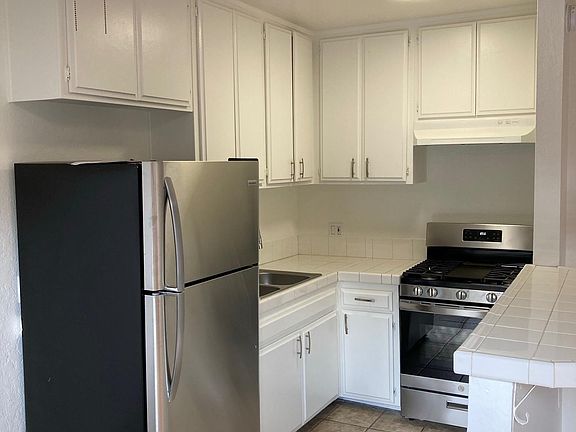 Modern kitchen with tile counters and flooring, ceiling fan above