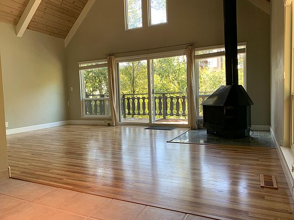 Living room with hard surface, wood burning stove, Attached deck with serene views, vaulted ceiling