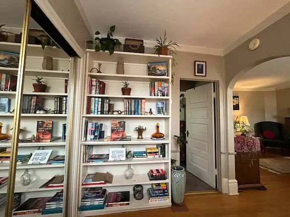 Private Reading Nook includes books, games, and chill vibes. Looking from couch towards Bathroom (door at center) and Bedroom (right, thru arch). Mirrored closet doors to left contain tons of storage for longer stays.