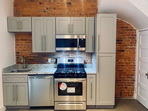 A new kitchen with stainless steel appliances, granite countertops, and an exposed brick wall.