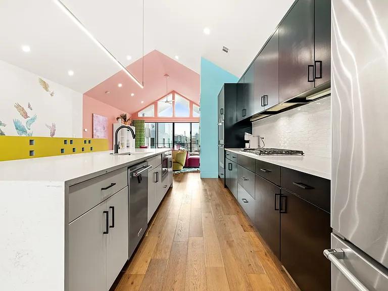 Open-concept kitchen with a large central island, light-finish countertops, stainless steel appliances, and wood-finish flooring