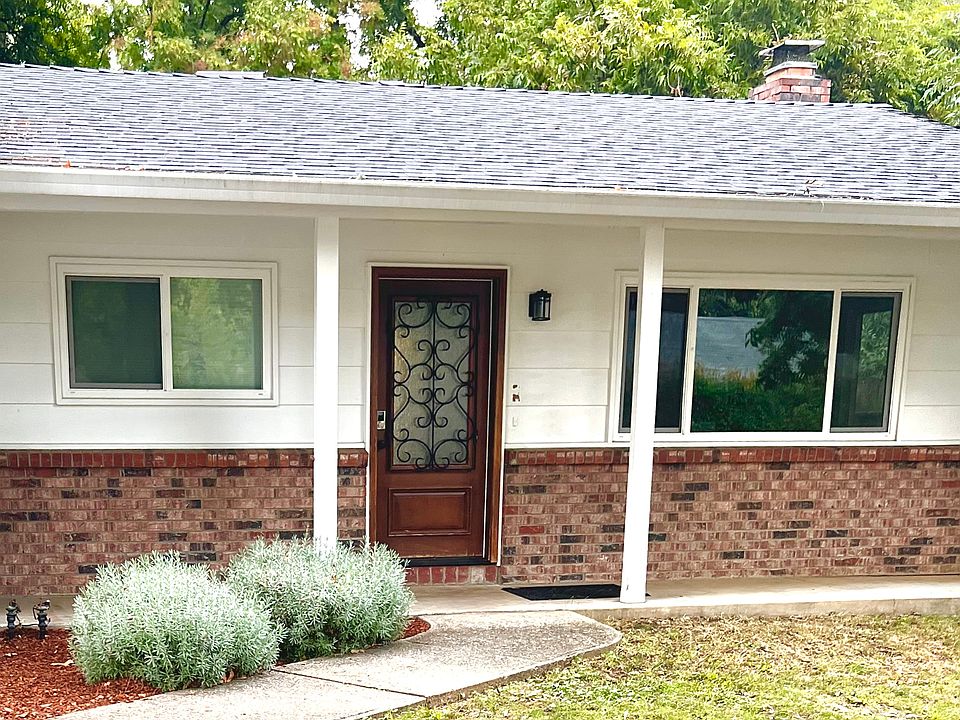 Front of home with covered porch, lush landscaping and large trees for shade