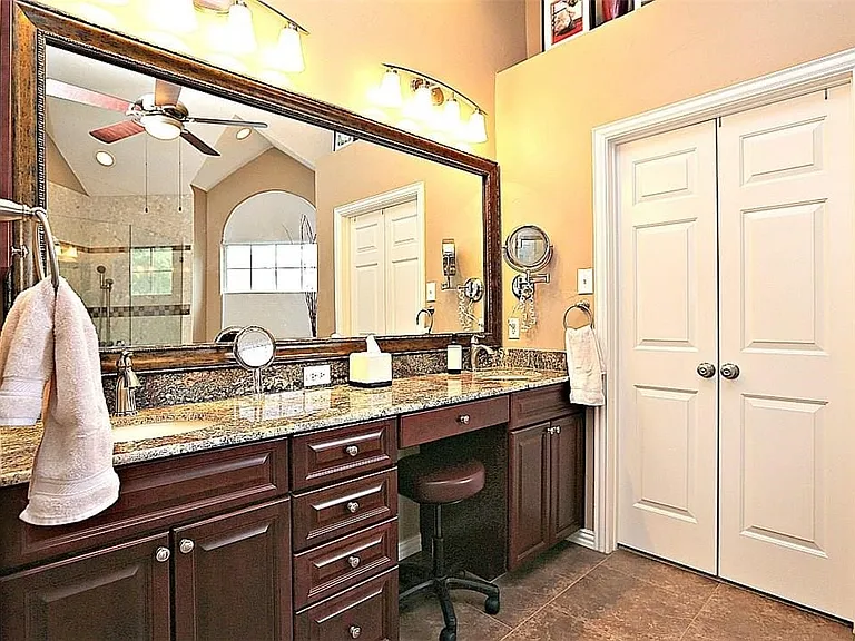 Bathroom featuring dual vanity with granite countertops, rich wood cabinetry, integrated dressing area, and a large framed mirror