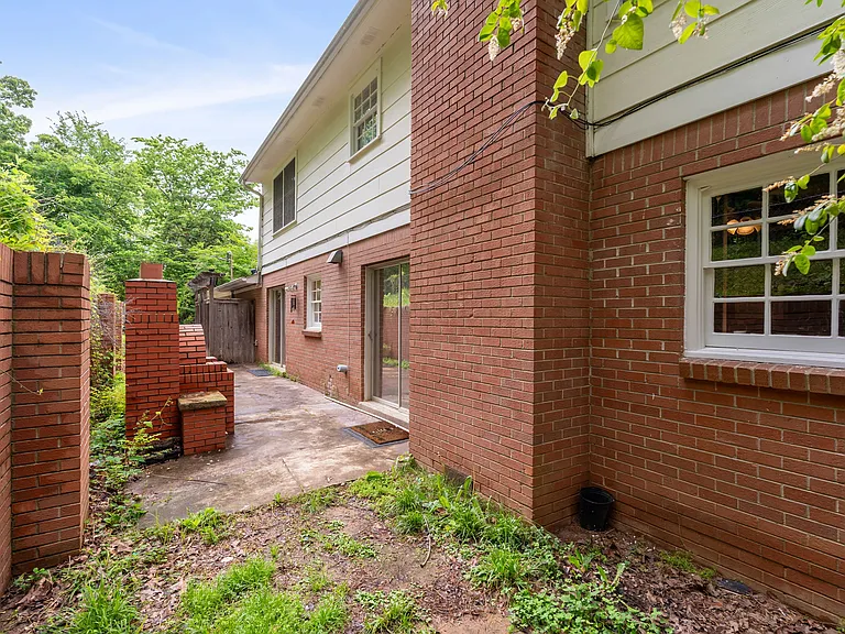 Back patio, includes raised garden bed, stunning and well-preserved retaining wall, two sliding door entry points, and a brick pizza, and grass dog run with wrought-iron fencing.