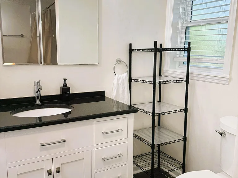 Bathroom with a large vanity, framed mirror lighting, and extra shelving, plus a window for ventilation and natural light.